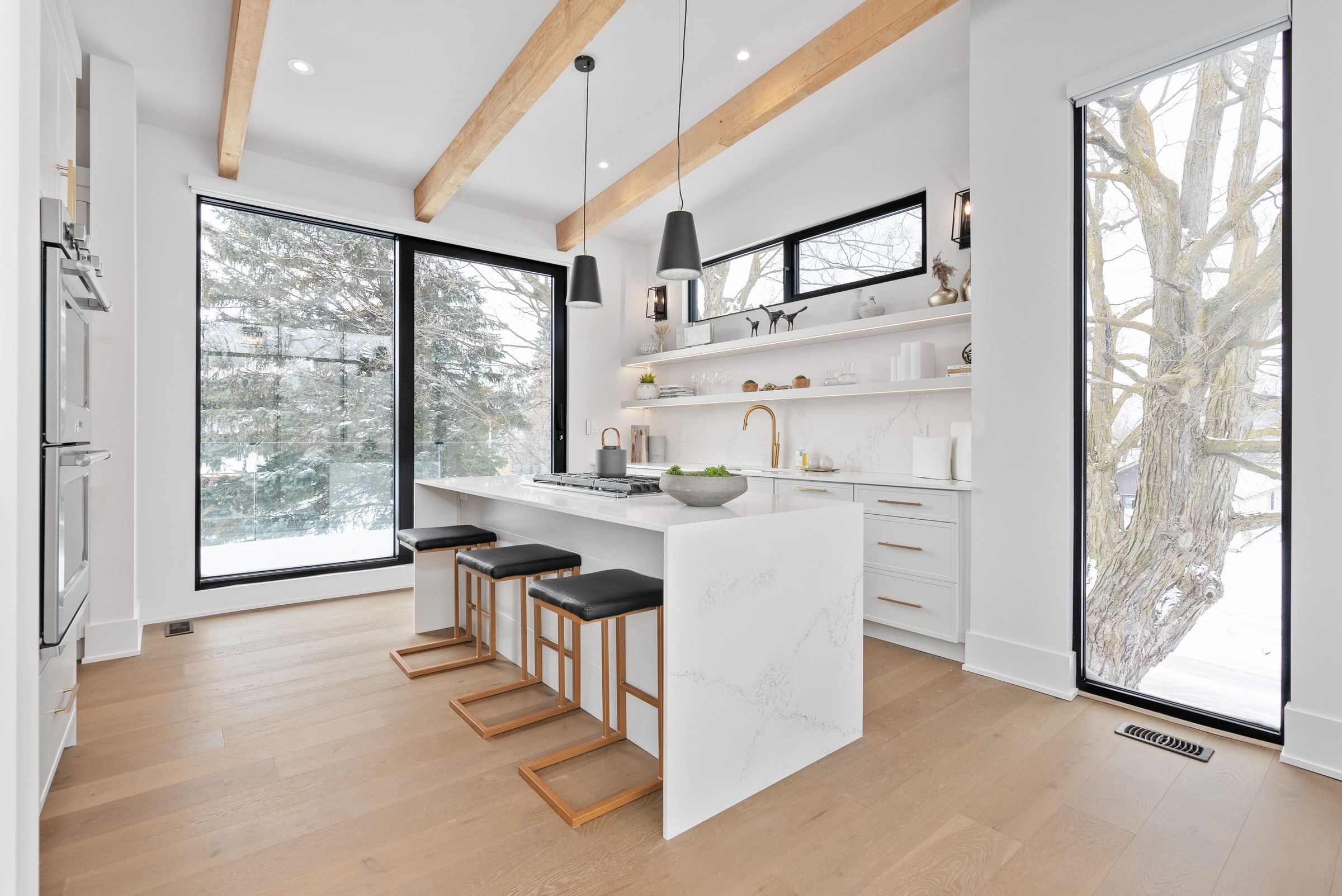 White quartz kitchen island with stools beneath exposed beams beside tall windows.