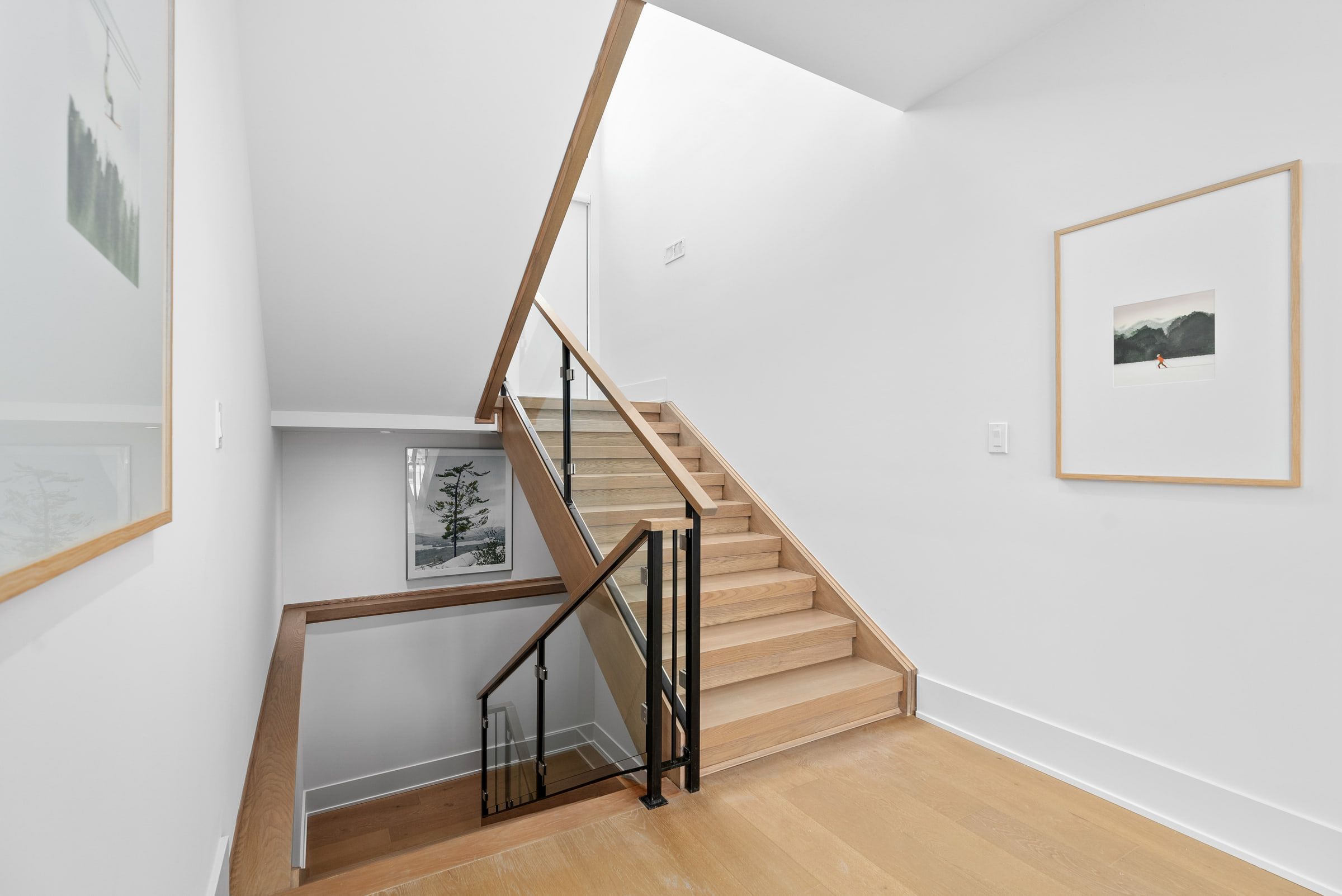 Oak stair treads and a black railing beside framed artwork.